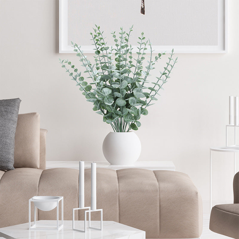 Frosted faux eucalyptus branches in a round white vase on a coffee table in a neutral modern living room